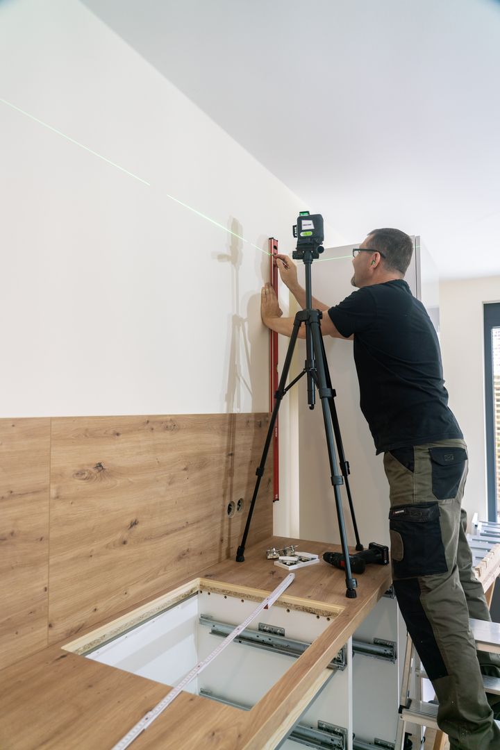 Handwerker richtet Hängeschrank mit Laser und Wasserwaage aus